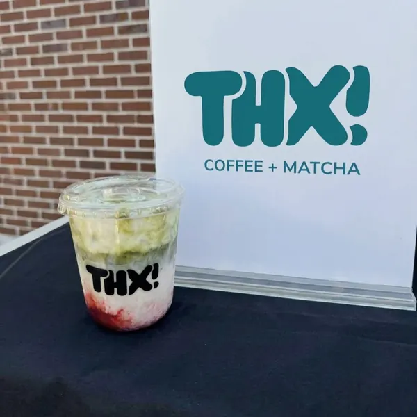 Iced strawberry matcha in a thx! cup in front of the thx! coffee + matcha sign