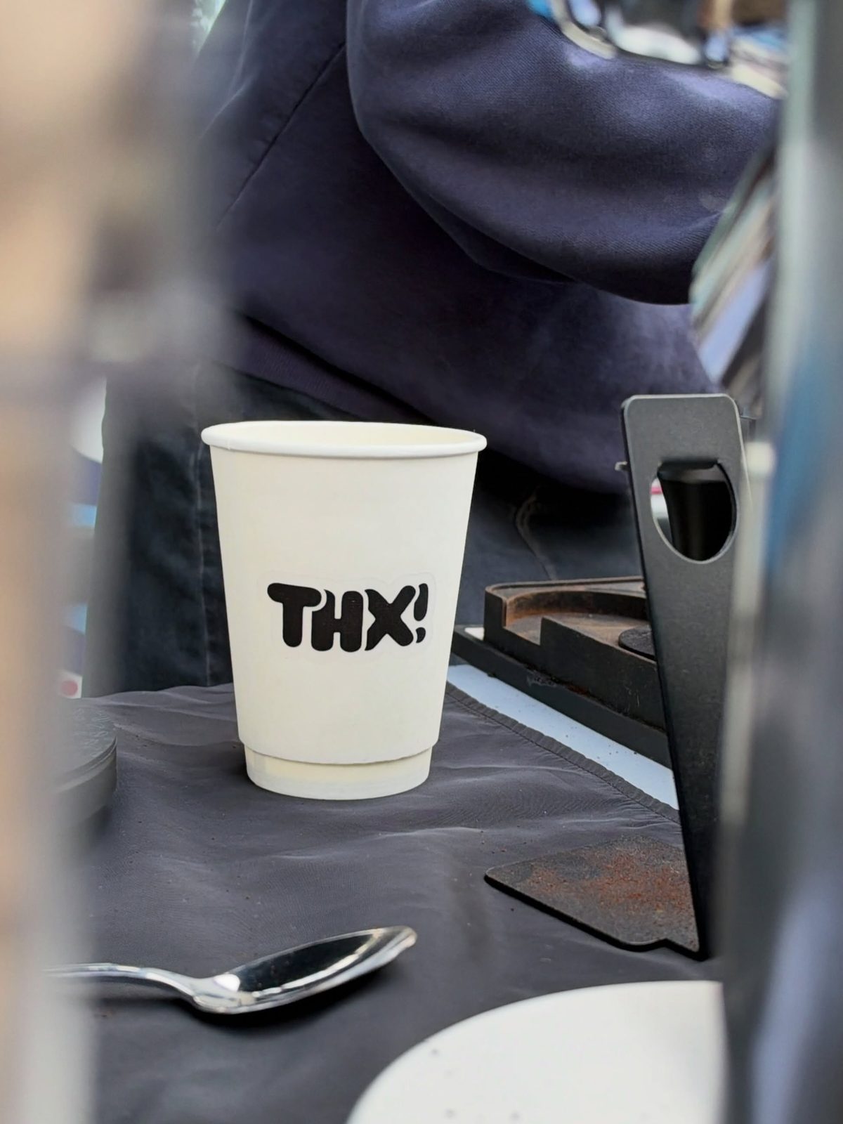 A white thx! paper cup on a black-draped table at our Federal Way Cars & Coffee pop-up